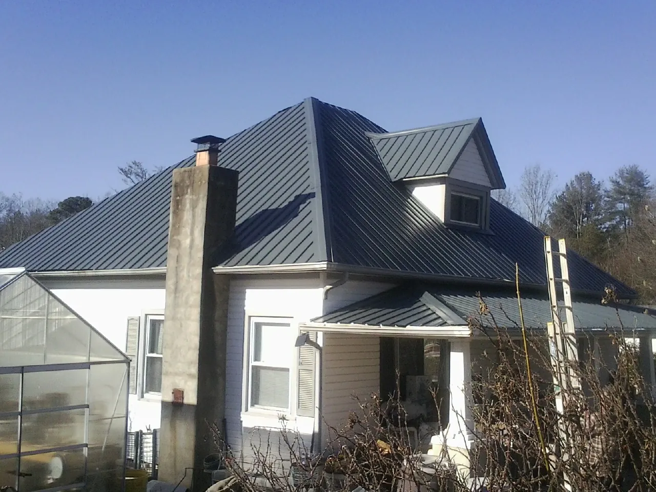 Dark blue standing seam metal roof on a white farmhouse with dormer — Slate & Tile Roof Repair by Roofing Brothers in Red Creek