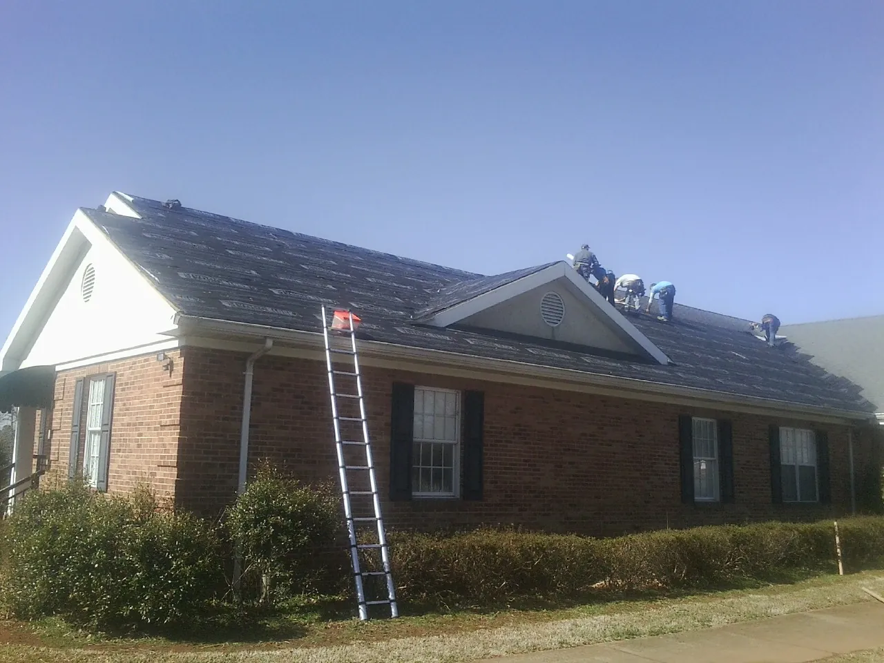 Crew tearing shingles off a brick ranch roof with a ladder set — Emergency Roof Repair work by our crew in Red Creek