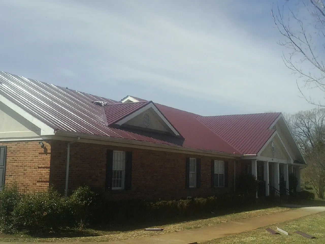 Red metal roof with gabled entries on a long brick building, from a Hail Damage Roof Repair job in Red Creek
