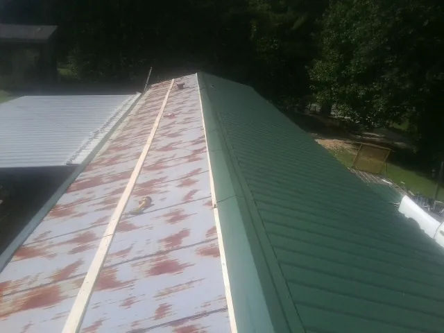 Old rusted panels beside newly installed green metal roofing — Wind Damage Roof Repair by Roofing Brothers in Red Creek