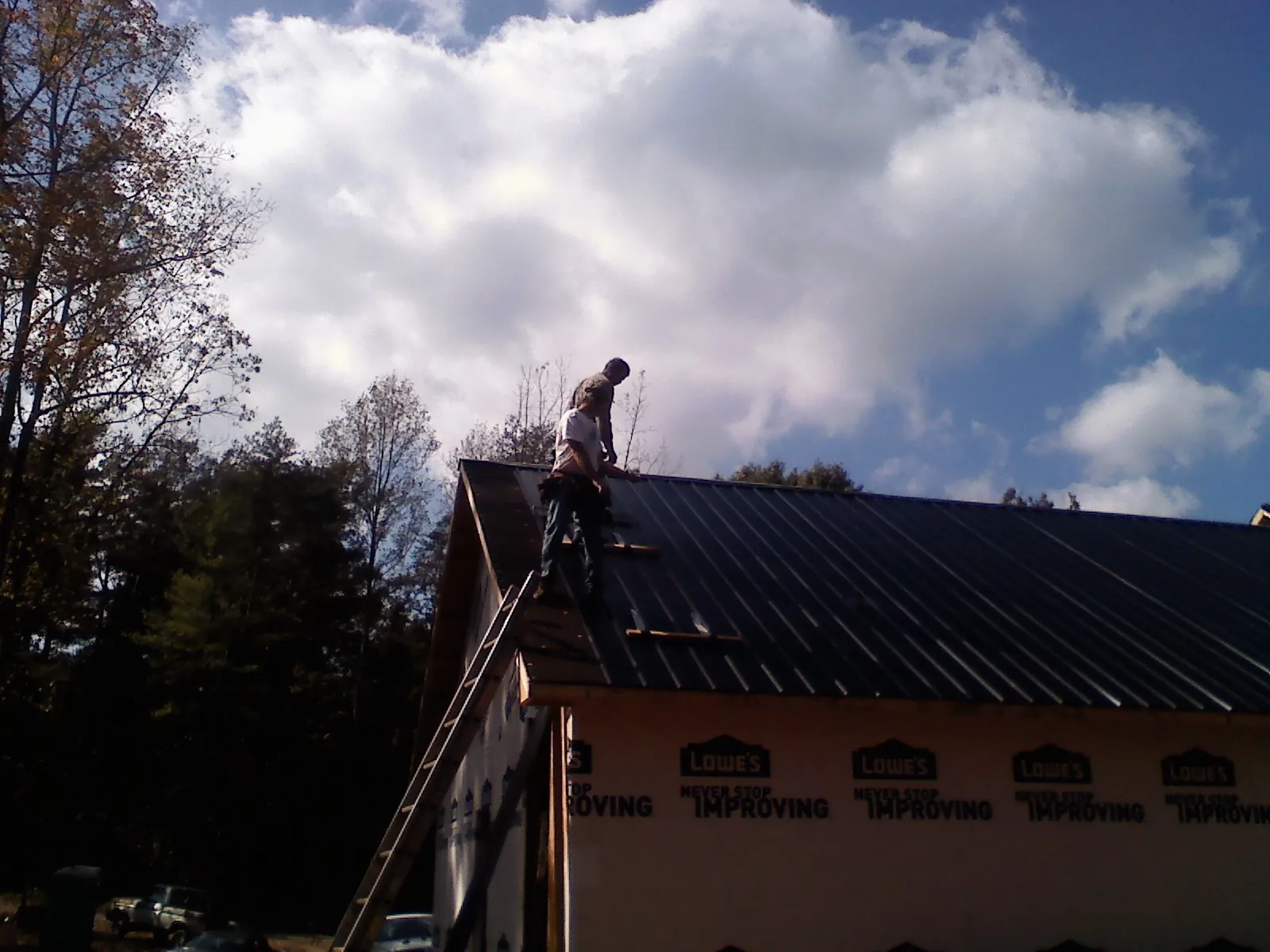 Roofer fastening dark metal panels high against a cloudy sky, from a Roof Inspection job in Red Creek