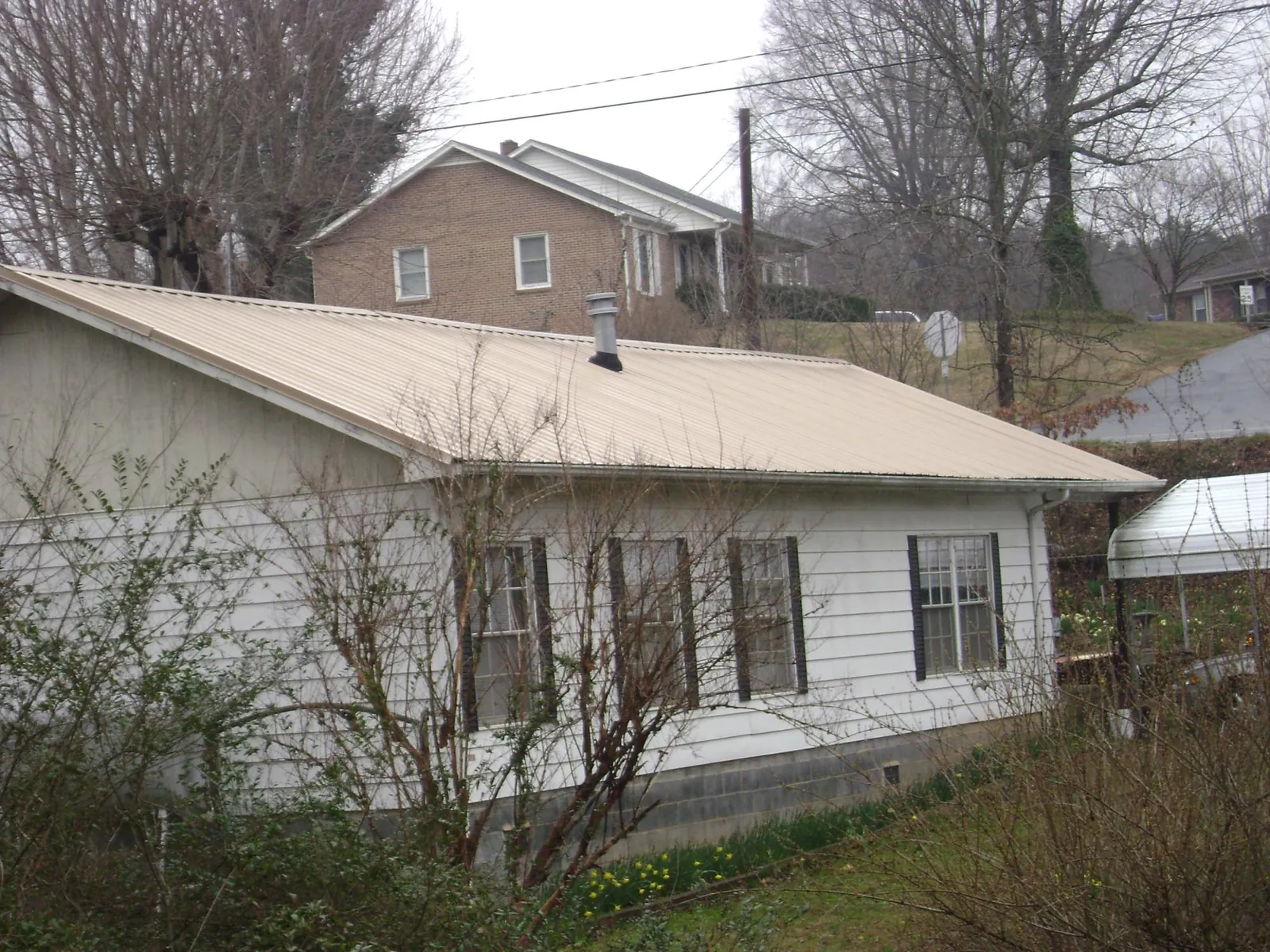 Tan metal roof on a white sided house set into a hillside — Commercial Roofing by Roofing Brothers in Red Creek