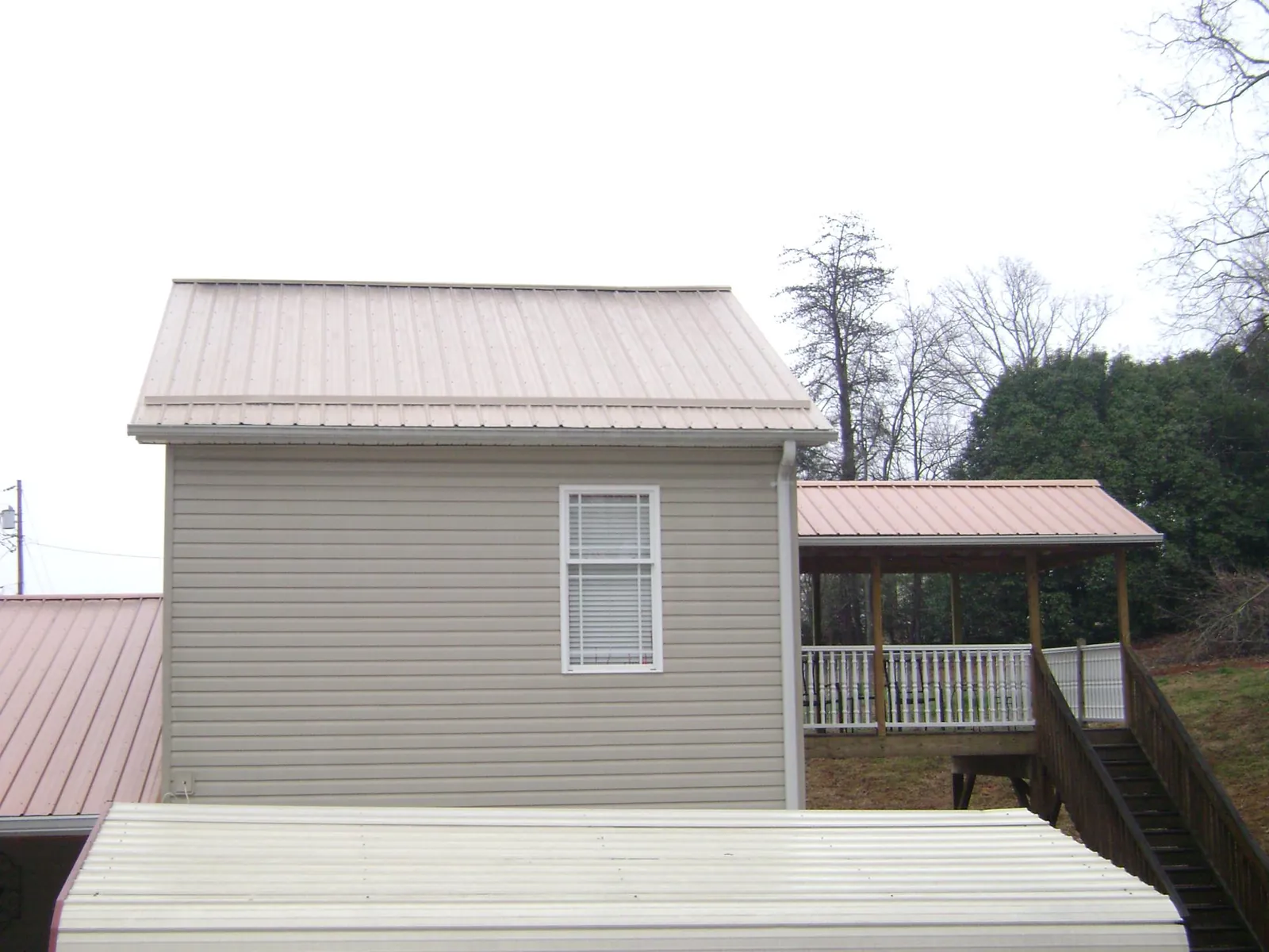 Tan metal roofs on a two story addition and attached porch, from a Roof Replacement job in Red Creek
